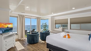 Una habitación de hotel moderna con una cama grande, televisión, escritorio y vista al océano.