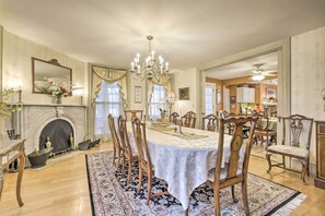 Uma sala de jantar com uma mesa grande, cadeiras, um lustre e uma lareira.