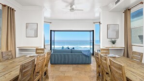 A room with a large window offering a view of the ocean, a ceiling fan, and wooden furniture. - Stunning Waterfront Oasis P823-1 (Oceanside)