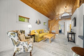 Amplia sala de estar con techo alto, un sofá amarillo, un sillón estampado y una mesa de centro de madera.