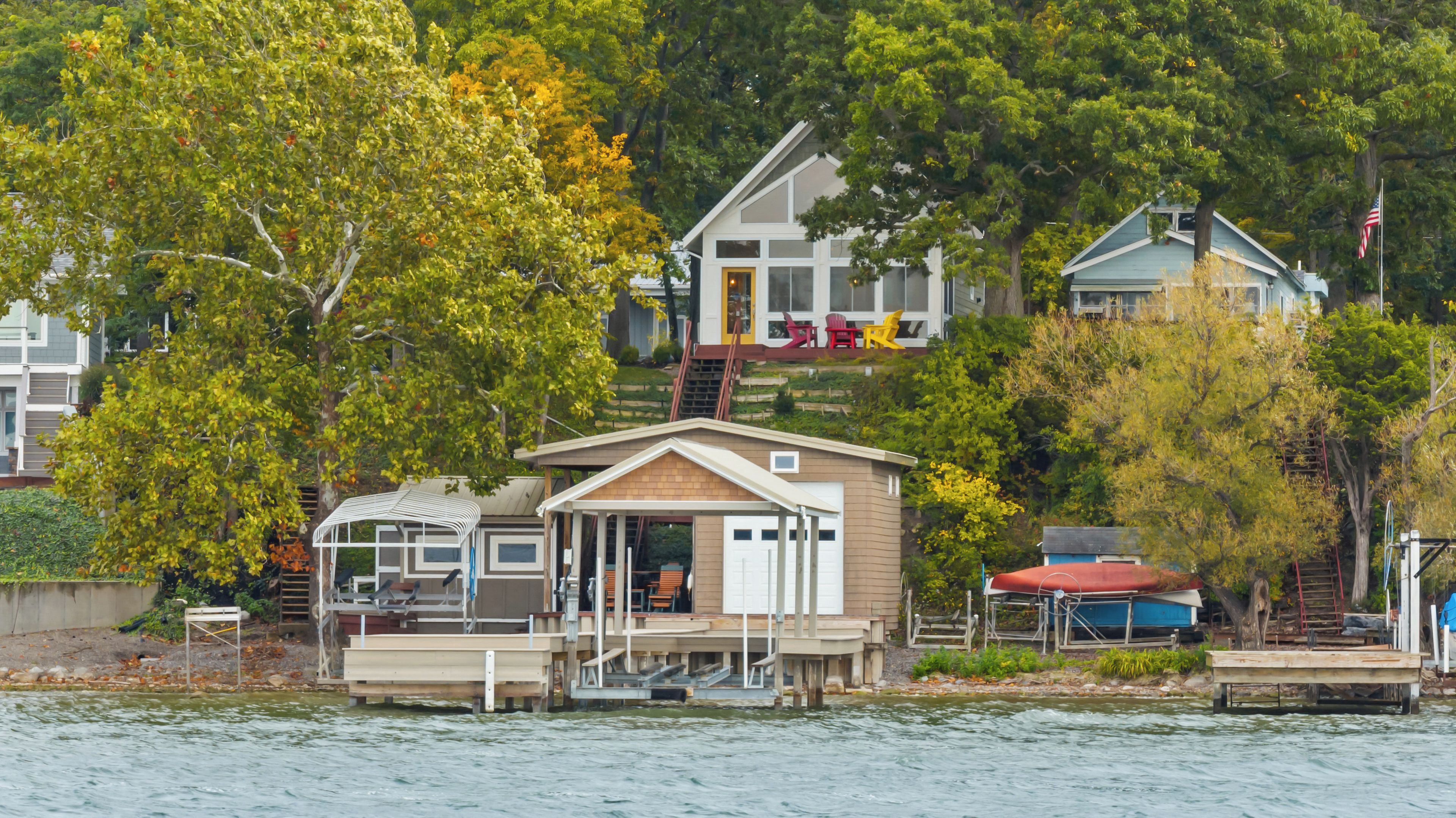 Un chalet au bord du lac, doté d’un quai, entouré d’arbres et d’autres maisons.