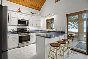 Una cocina moderna con armarios blancos, electrodomésticos de acero inoxidable, una isla grande con taburetes y vistas al exterior a través de un ventanal.