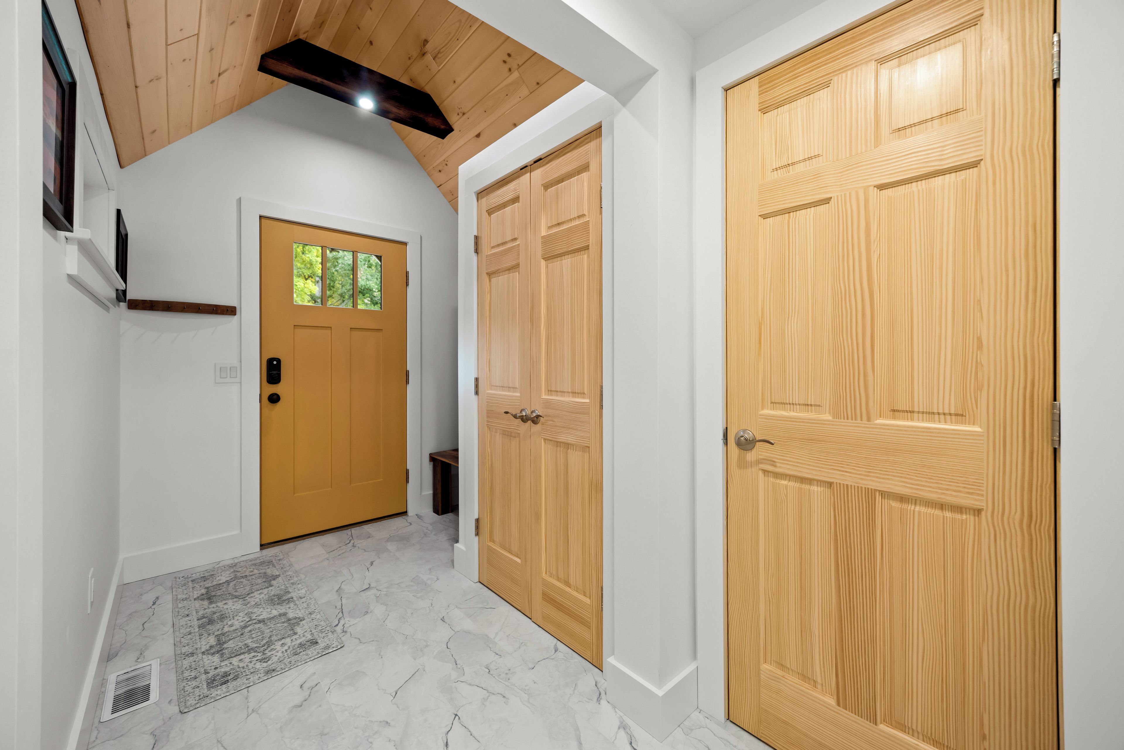 A hallway with two wooden doors, one with a window, and a marble floor.
