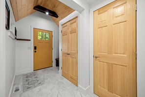 Un pasillo con dos puertas de madera, una con ventanal, y piso de mármol.