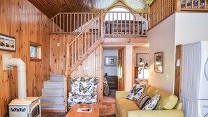 Interior acogedor de una cabaña con escalera de madera, un sofá, una mesa y una estufa.