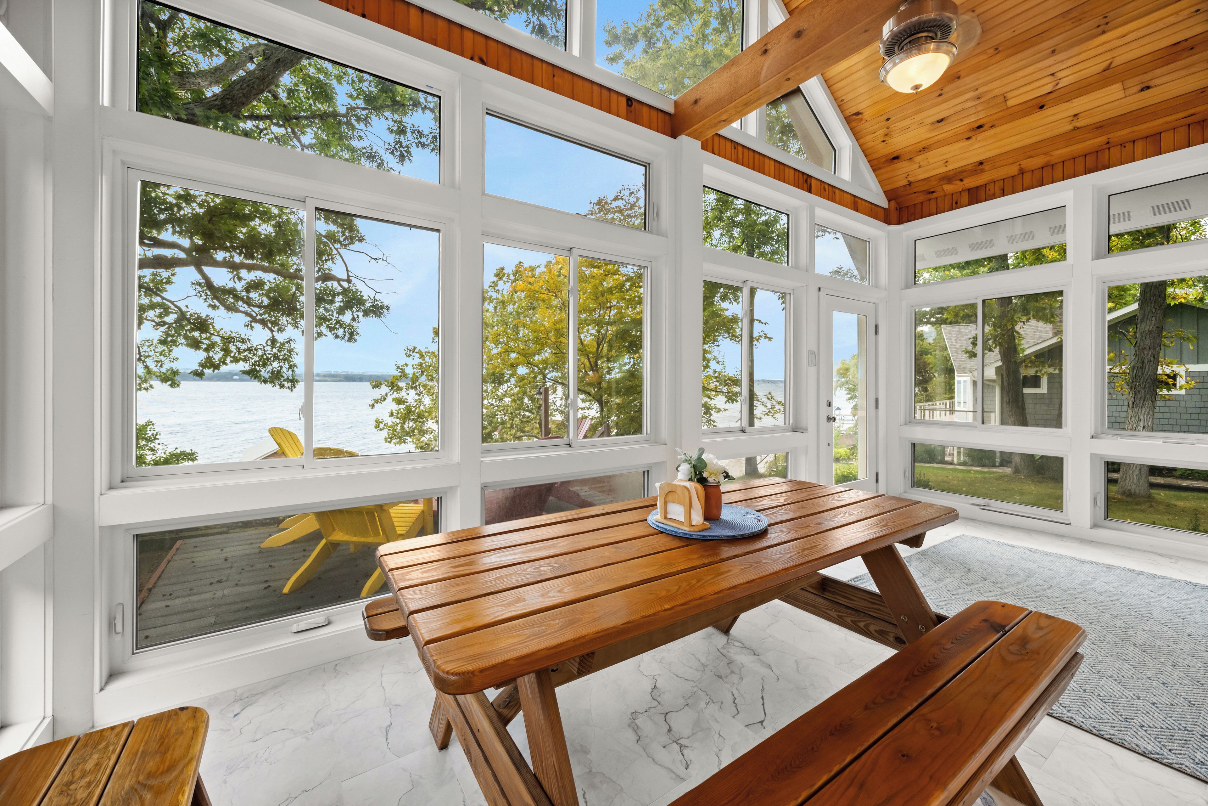 A wooden deck with a table and benches, overlooking a body of water and trees.