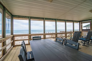 Una terraza techada con vista al océano, muebles de madera y barandilla.