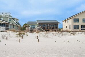 Una proprietà fronte spiaggia con spiaggia sabbiosa, una scala in legno che conduce a una casa e un'ampia terrazza.