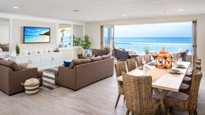 Ett modernt vardagsrum med ett stort fönster med utsikt över havet, inrett med en soffa, ett matbord och flätade stolar.