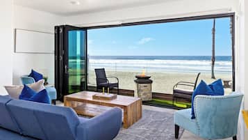 Una sala de estar moderna con un gran ventanal que da a un balcón con vistas a la playa.