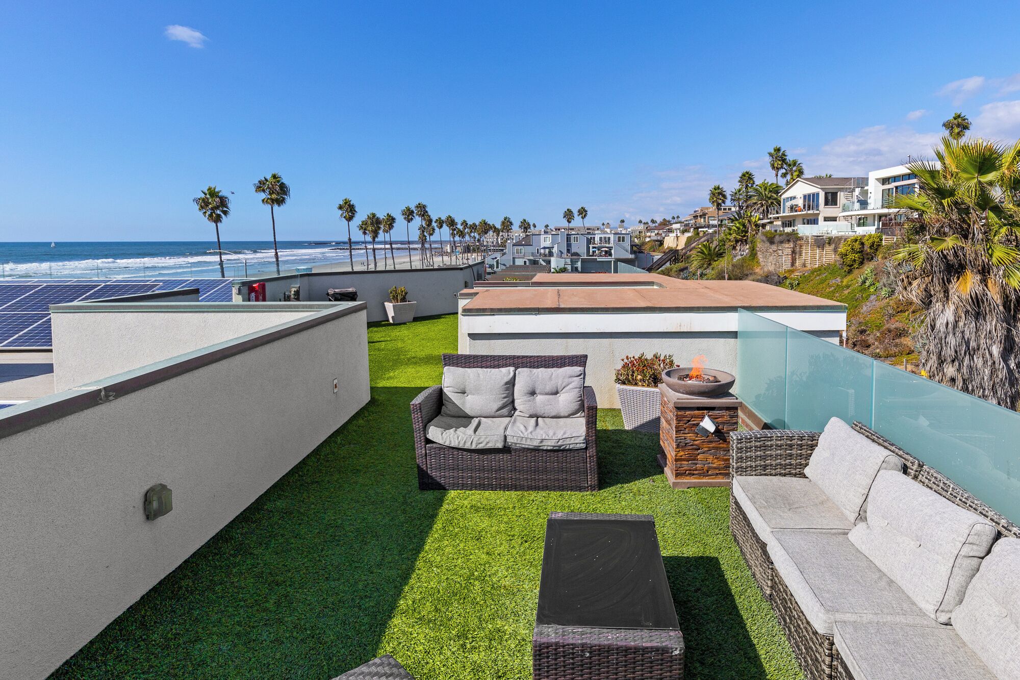 A rooftop patio with artificial grass, wicker furniture, and a fire pit.