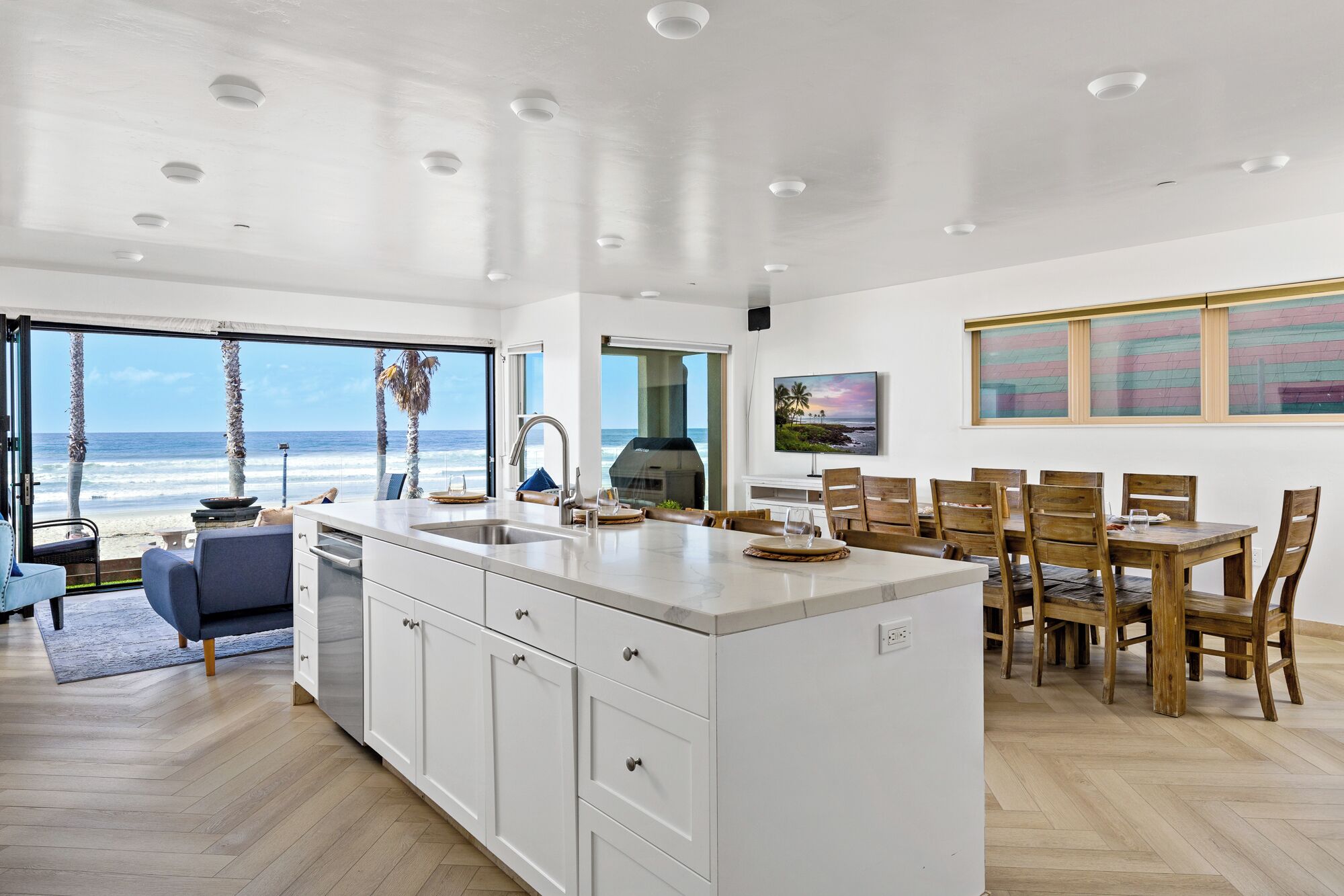 A spacious kitchen with a large island, a dining area with wooden chairs, and a view of the ocean through large windows.