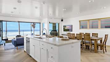 A spacious kitchen with a large island, a dining area with wooden chairs, and a view of the ocean through large windows.