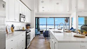 A modern kitchen with white cabinetry, a central island, and a view of the ocean. - Beachfront Bliss - Panoramic Doors & Beach Access - 702-1 (Oceanside)
