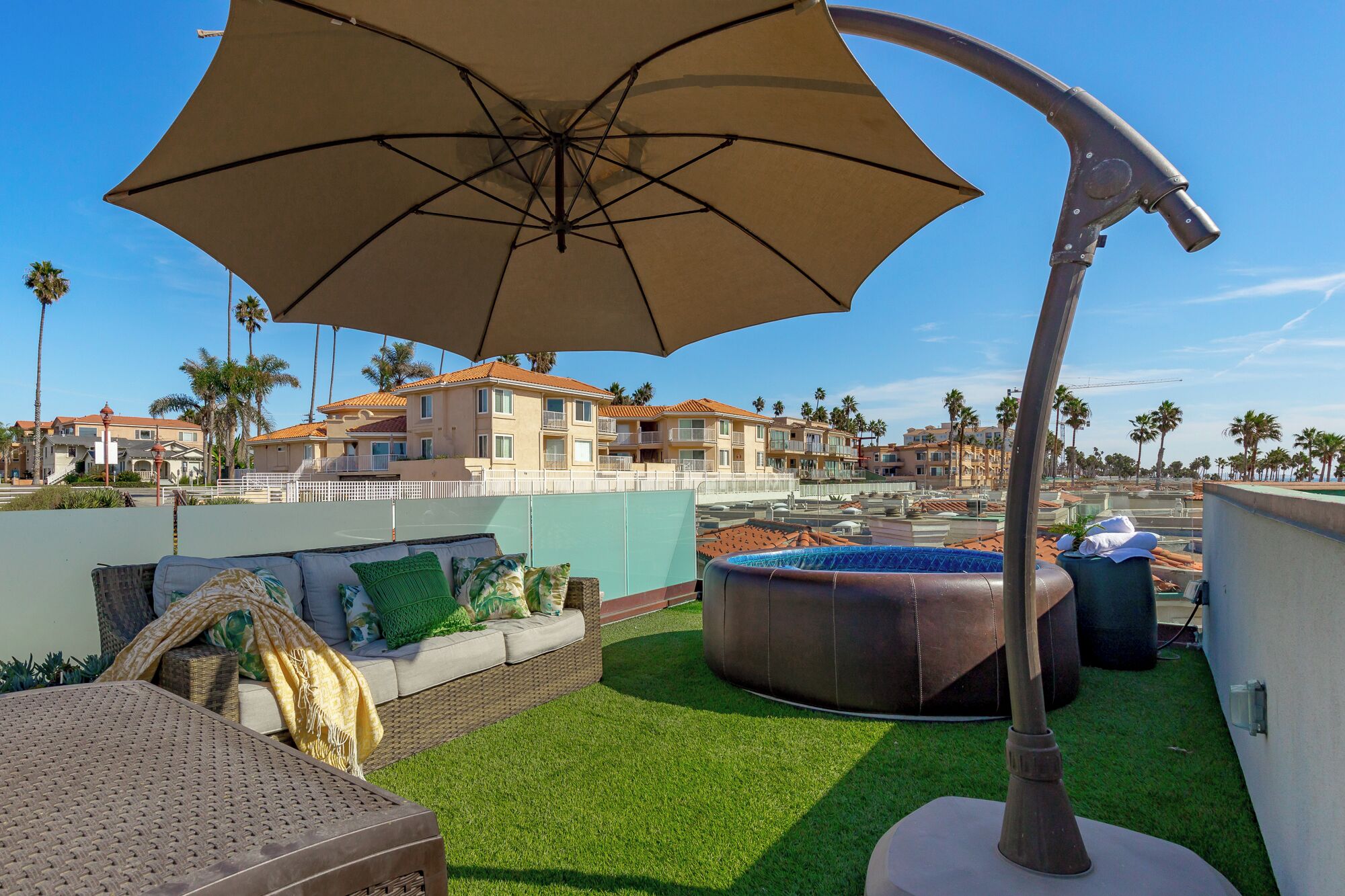 A rooftop patio with a large umbrella, a hot tub, and a wicker sofa.