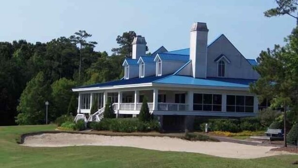 A large, two-story house with a blue roof and white exterior, surrounded by a well-maintained lawn and trees.