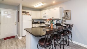 A modern kitchen with white cabinets, a black countertop, and a central island with bar stools.