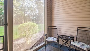 A covered porch with two chairs and a view of a grassy area and trees.