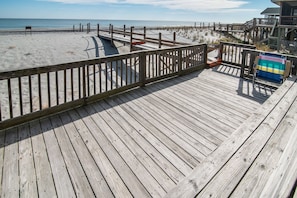 A wooden boardwalk leading to a sandy beach with a wooden fence and a beach chair.