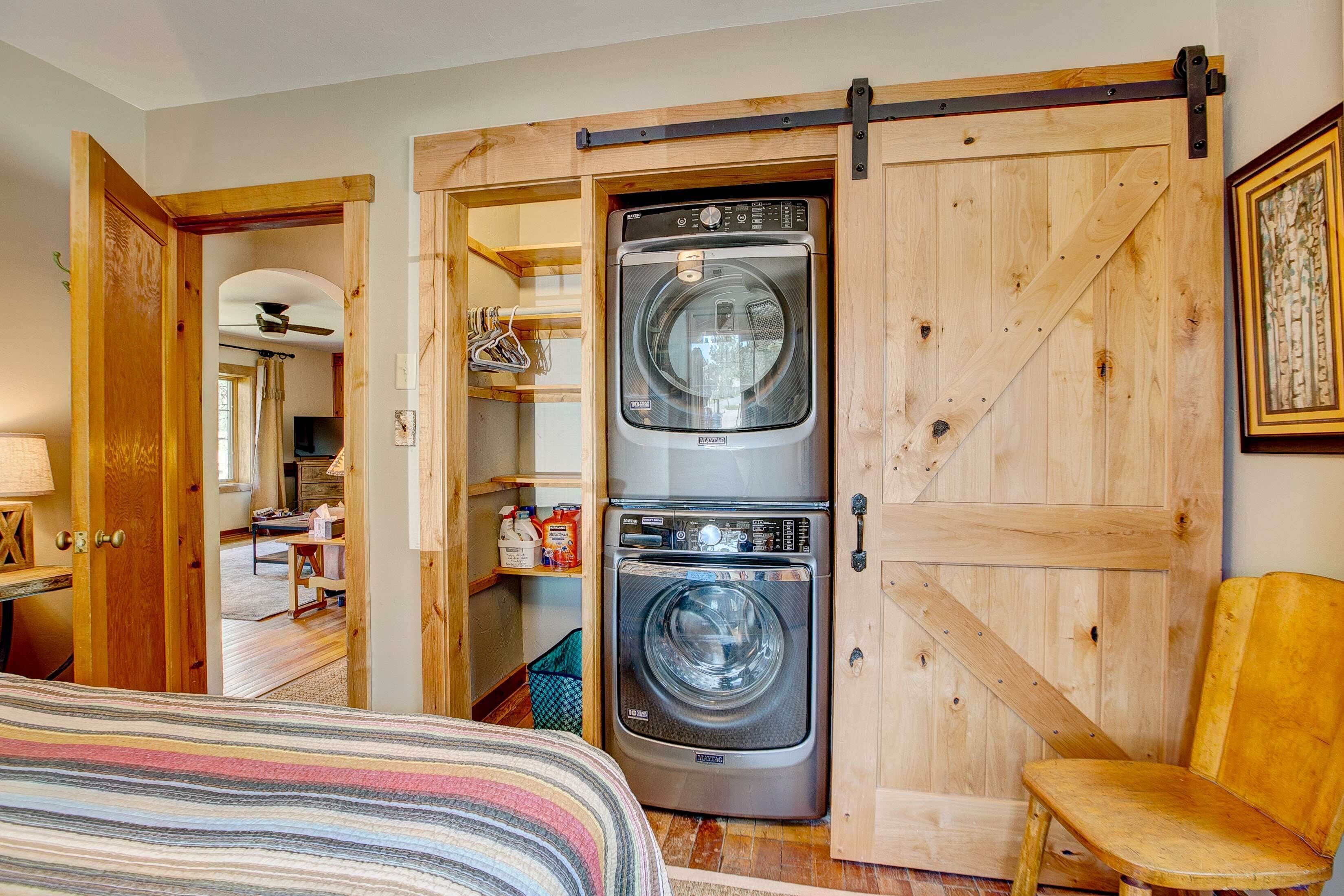 A laundry room with two stacked front-loading washers and dryers, wooden sliding doors, and a chair.