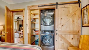 A laundry room with two stacked front-loading washers and dryers, wooden sliding doors, and a chair. - Charming Estes Park Cabin w/ 2 Private Patios! (Estes Park)