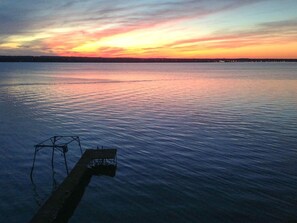 Eine Steg, der sich in ruhiges Wasser erstreckt, mit einem Sonnenuntergang im Hintergrund.