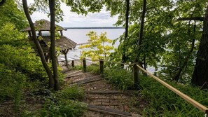 A wooden staircase leading to a gazebo by a lake, surrounded by lush greenery.