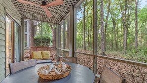 Un espace extérieur abrité, avec une table et des chaises, un ventilateur de plafond et une vue sur une forêt.