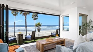 Ein modernes Wohnzimmer mit einem großen Glasfenster, das auf einen Balkon mit Blick auf einen Strand führt.