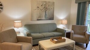 Een woonkamer met een bank, twee fauteuils, een salontafel en een schilderij aan de muur.