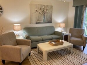 A living room with a sofa, two armchairs, a coffee table, and a painting on the wall.
