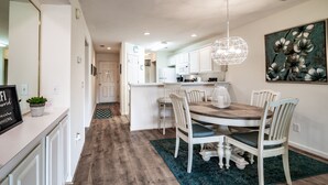 Een moderne keuken met witte kasten, een centraal eiland en een eethoek met een houten tafel en witte stoelen.
