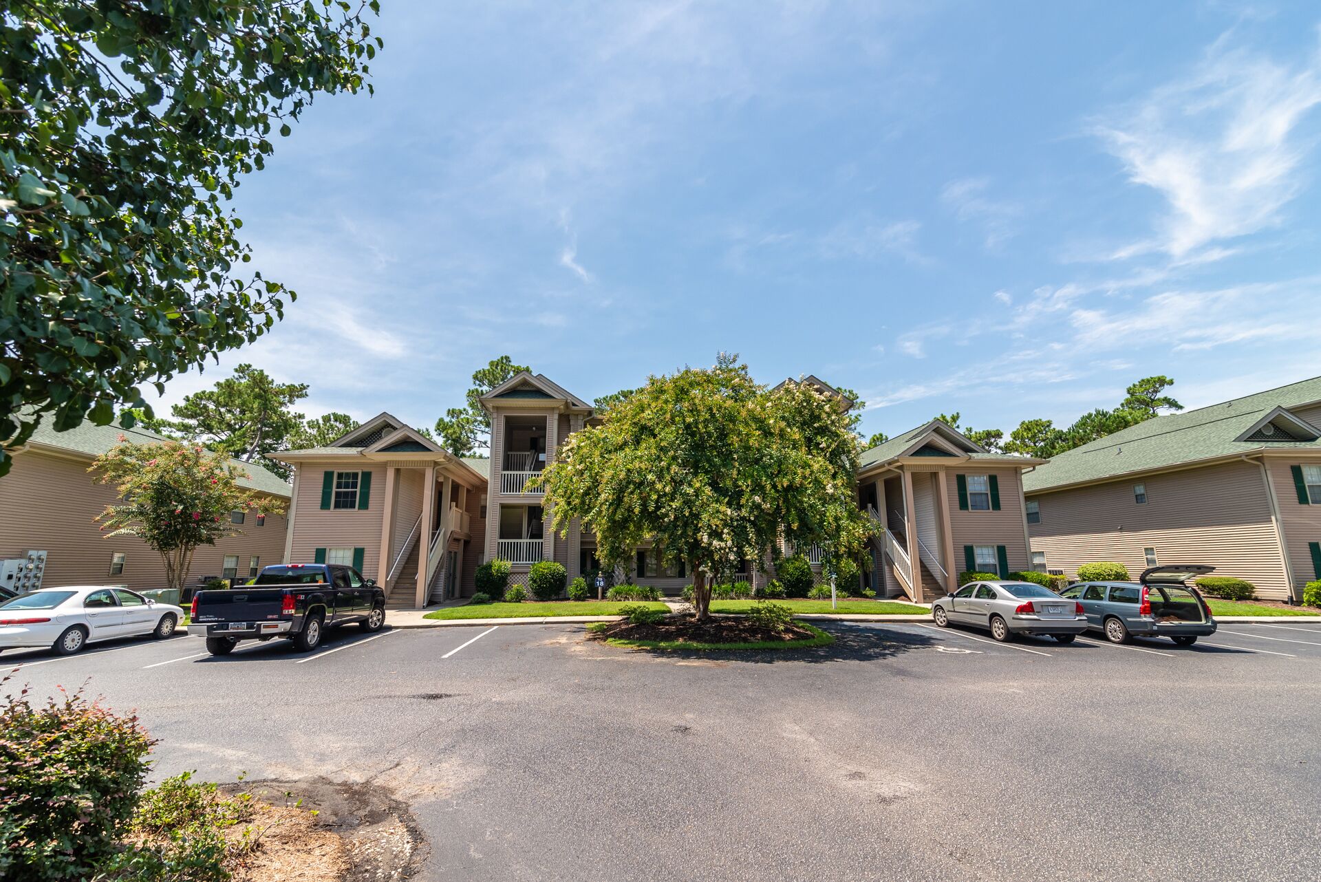 A multi-story residential building with a central courtyard, parking lot, and surrounding greenery.