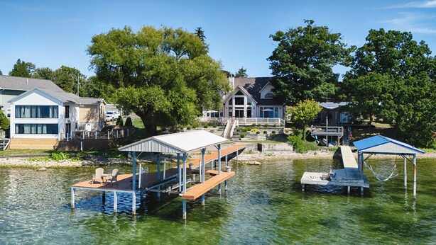 A lakeside property with a dock, a covered seating area, and a house with a large deck. - Five Gates: Lakeside Paradise! Seneca Lake Luxury Home! (Geneva)