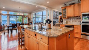 A spacious kitchen with a large island, wooden cabinets, and a stone fireplace. - Five Gates: Lakeside Paradise! Seneca Lake Luxury Home! (Geneva)