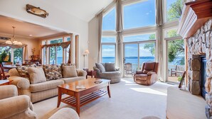 A spacious living room with a large window overlooking a scenic view, a cozy seating area, and a stone fireplace. - Five Gates: Lakeside Paradise! Seneca Lake Luxury Home! (Geneva)