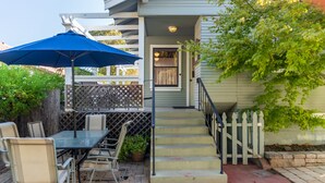 A patio with a table and chairs, a blue umbrella, and a staircase leading to a door. - 1916 Craftsman + Firepit | Walk Downtown | Poe House (Paso Robles)