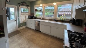 A kitchen with a stove, sink, and window with curtains. - 1916 Craftsman + Firepit | Walk Downtown | Poe House (Paso Robles)