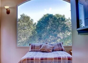 A bedroom with a large window, a bed with a plaid bedspread, and a wall-mounted light fixture.