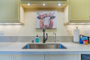 A kitchen with a stainless steel sink, a faucet, a soap dispenser, and a decorative painting above the sink. - Private Deck + Ping Pong + Farmhouse Kitchen | Paso Wine Country | Vin Rouge 51 (Paso Robles)