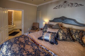 Een slaapkamer met een groot bed, een stoel en een badkamer door een open deur zichtbaar.