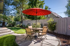 Une terrasse avec une table ronde et quatre chaises, un parasol rouge et une clôture en bois en arrière-plan.