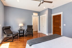 Une chambre à coucher comprenant un lit, deux chaises, une petite table avec une lampe, un ventilateur de plafond et une armoire.