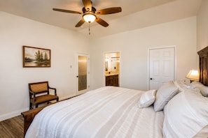 A bedroom with a bed, a chair, a ceiling fan, and a door leading to a bathroom.