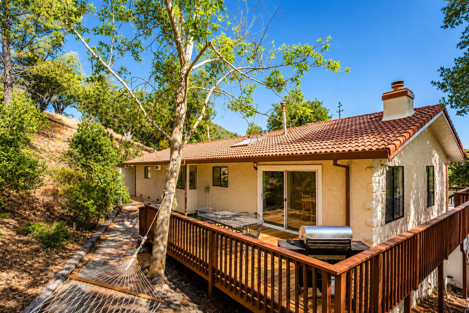 A two-story house with a patio, a barbecue grill, and a wooden deck.