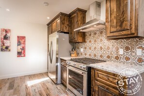 Une cuisine avec des meubles en bois, un réfrigérateur en acier inoxydable, une cuisinière et un crédence décorée.