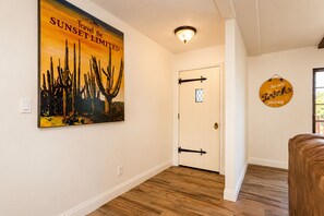 Un pasillo con suelo de madera, una puerta con ventanal y una pared con un cartel y un letrero.