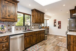Una cocina con armarios de madera, lavavajillas de acero inoxidable y un ventanal amplio.
