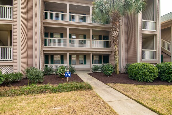 A multi-story residential building with balconies, a palm tree, and a pathway leading to the entrance. - TB 13D 3Br/3Bath unit super nice with great view on golf course (Pawleys)
