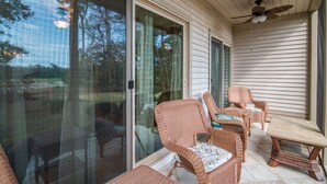 Una veranda coperta con mobili in vimini, una ventola a soffitto e una porta scorrevole che dà su un giardino.